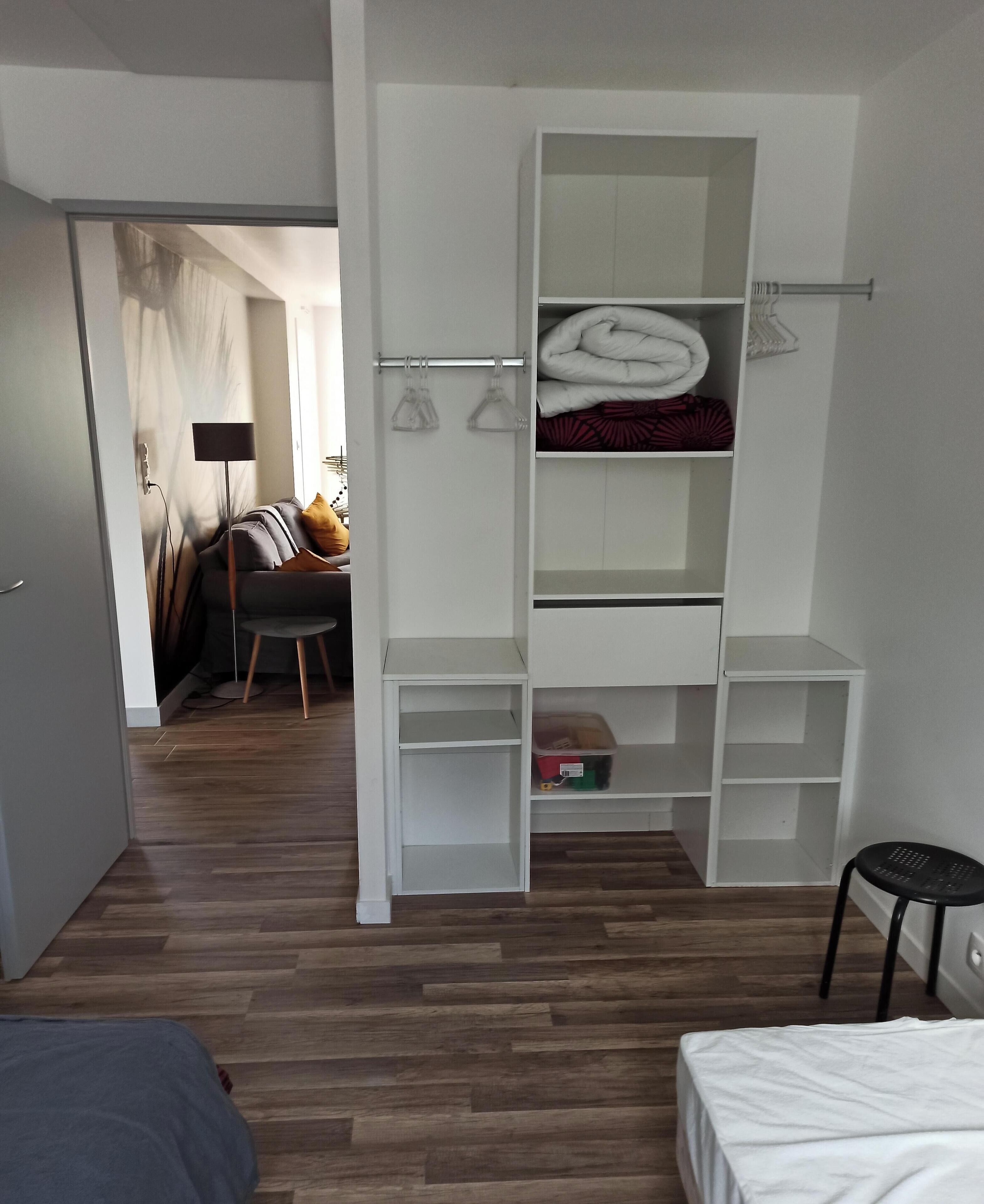A modern, well-lit room with a wooden floor, a white bed, and a white wardrobe with multiple compartments.