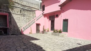 Un patio con piso de piedra, un edificio rosa con una escalera y un muro de piedra.