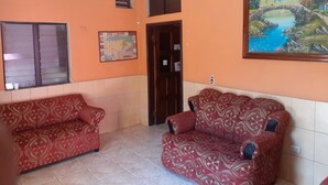 Una habitación con dos sofás estampados, un ventilador de techo, un mapa en la pared y un cuadro de un paisaje.