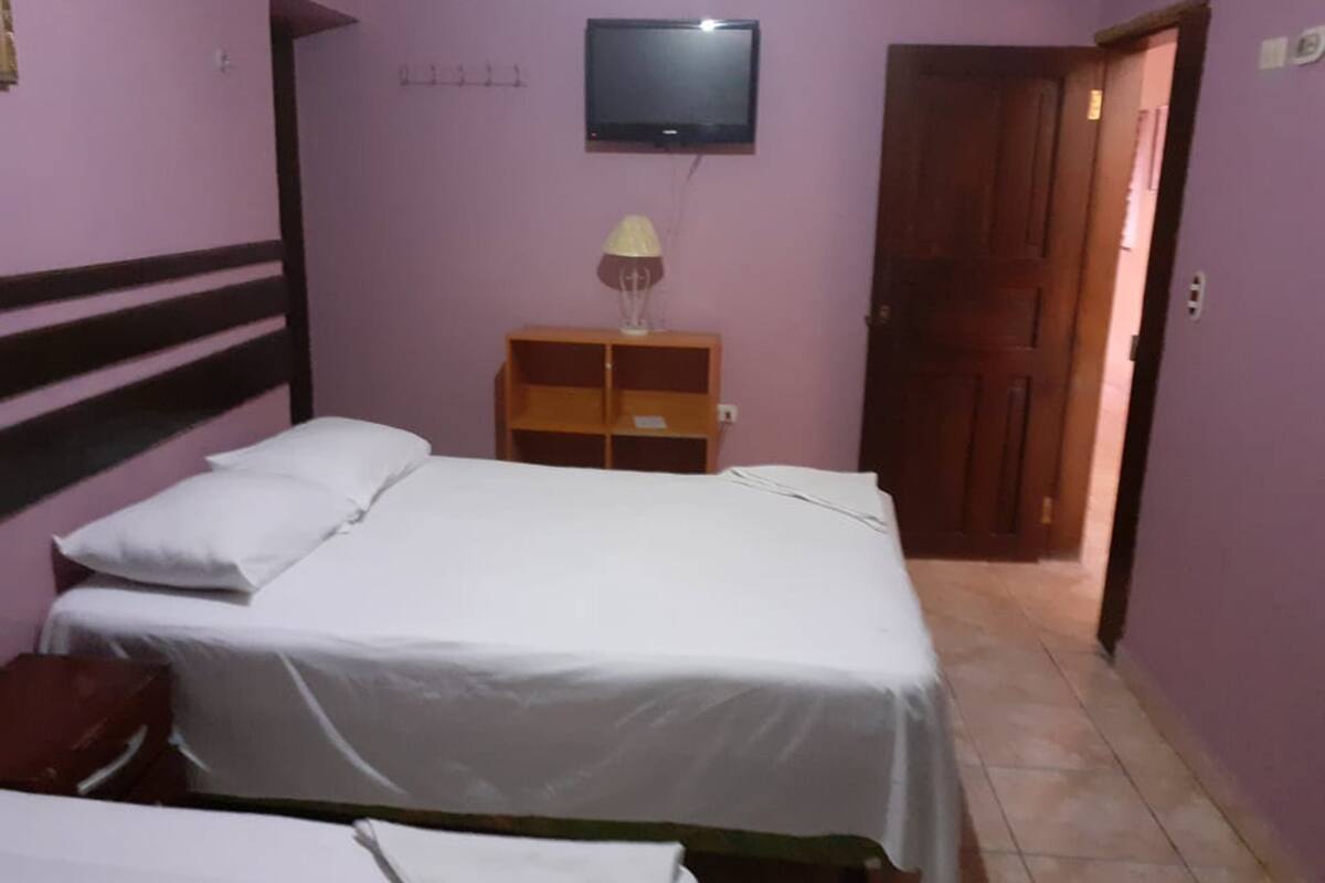 A room with two beds, a TV mounted on the wall, and a wooden door.