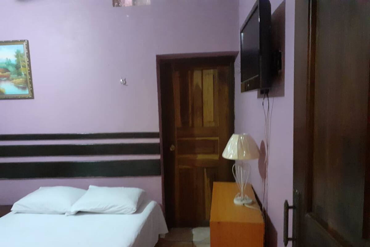 A bedroom with a bed, a television mounted on the wall, and a wooden door.