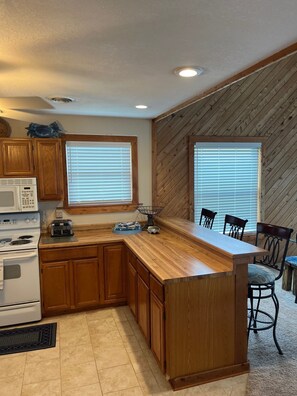 A kitchen with wooden cabinets, a microwave, a stove, and a dining area with chairs and a table.