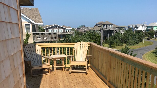 Een houten terras met twee Adirondack-stoelen en een tafeltje, met uitzicht op een woonwijk.