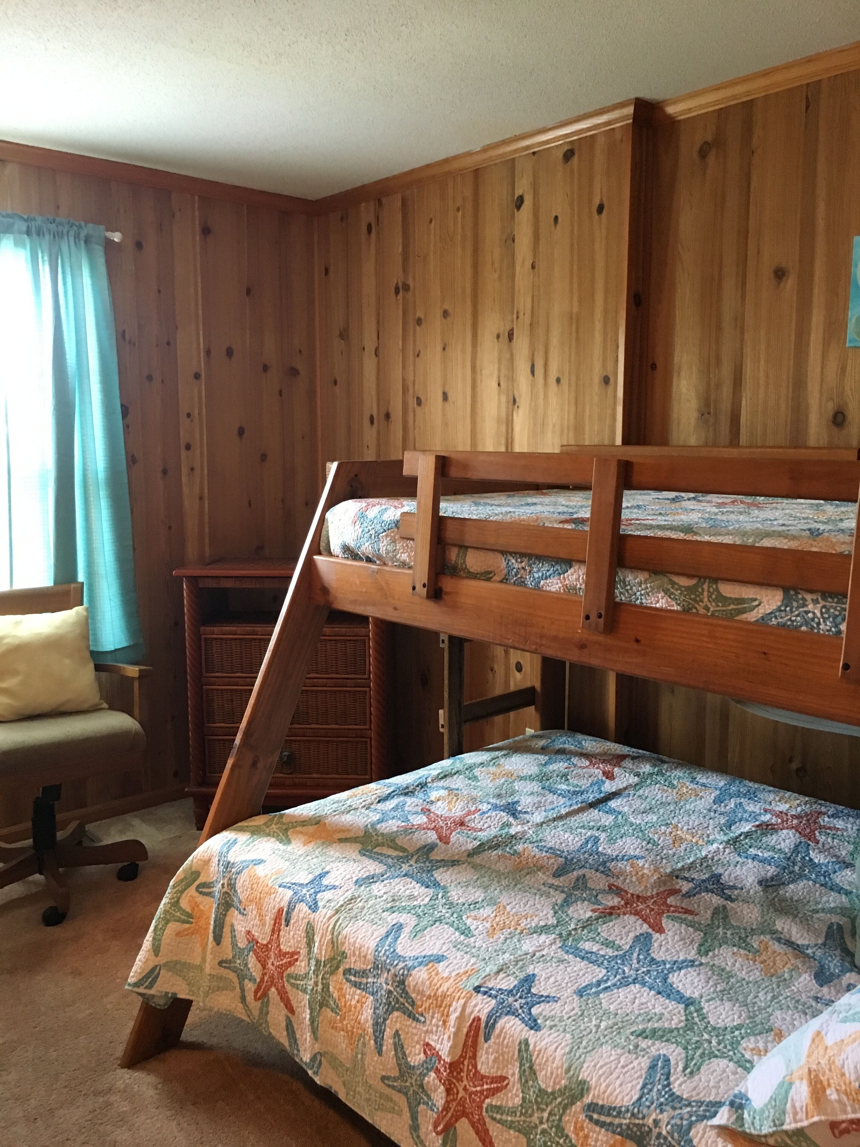 A bunk bed room with a wooden wall, a desk, and a chair.