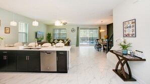 A spacious kitchen with a central island, dark cabinetry, and a dishwasher. There is a dining area with a table and chairs, and a staircase leading to an upper level. - Serenity by Your Private Pool! No Rear Neighbors! Resort Near DISNEY! (Kissimmee)