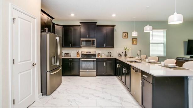 A modern kitchen with dark cabinets, stainless steel appliances, and a marble floor. - Serenity by Your Private Pool! No Rear Neighbors! Resort Near DISNEY! (Kissimmee)