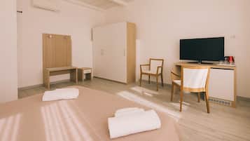 Una habitación de hotel con una cama, un escritorio con computadora, una silla, un televisor y un armario.