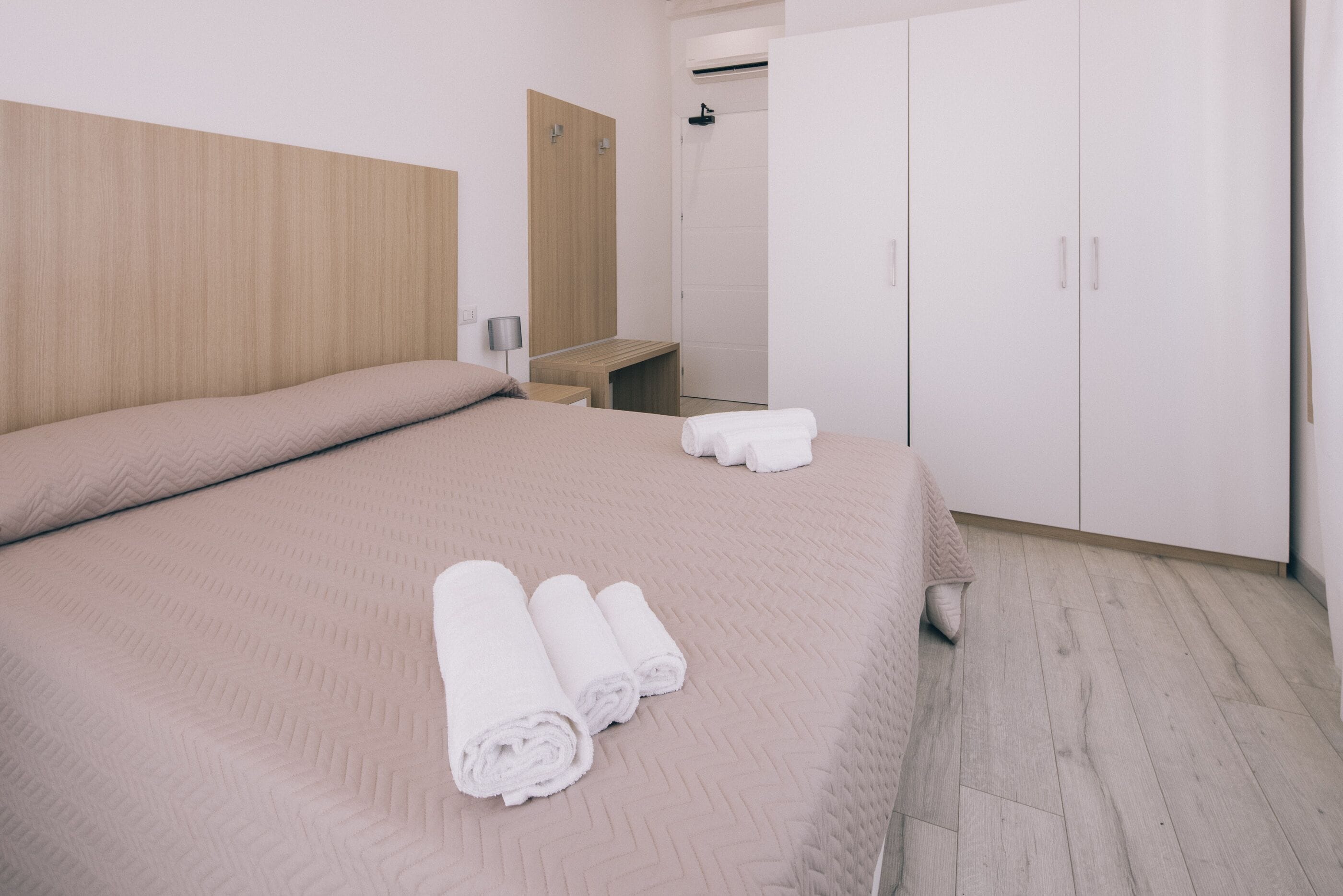 A hotel room with a large bed, a wooden headboard, a wardrobe, and a bench.