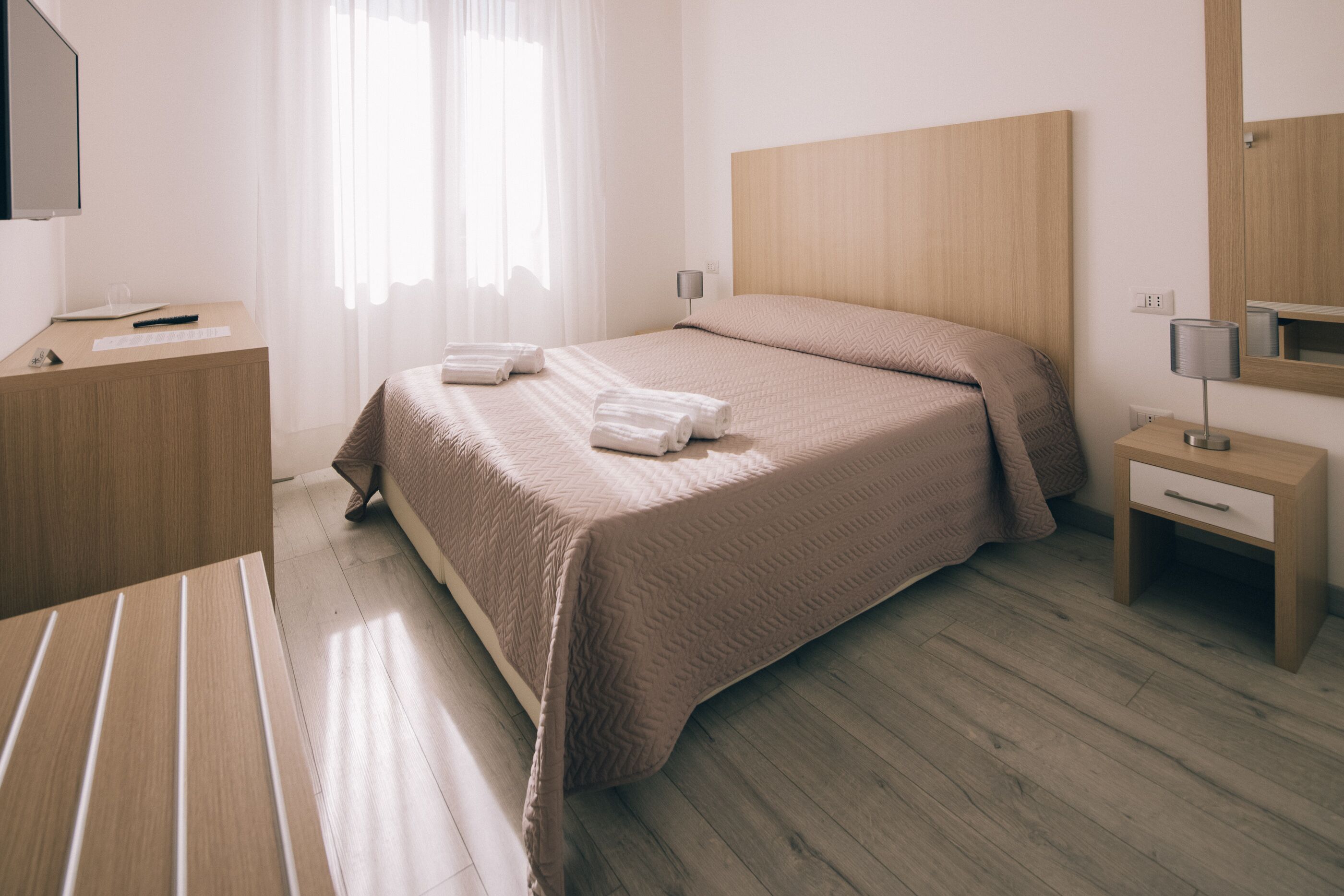 Una habitación de hotel con una cama grande, mesitas de noche, un escritorio y un espejo.