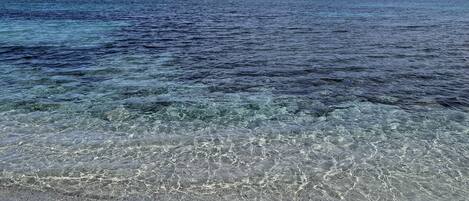 Una playa con agua cristalina, una isla rocosa en la distancia y una pequeña península con árboles.