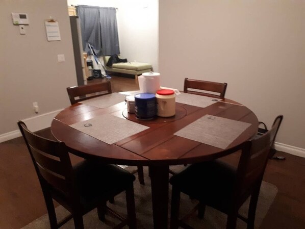 Una mesa de madera redonda con cuatro sillas, una lámpara de mesa pequeña y algunos documentos enrollados sobre la mesa.