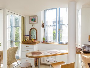 A bright kitchen with a wooden table, wicker chairs, and a large window with blue curtains.