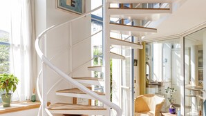 A spiral staircase with wooden steps and white railings, leading to a bright room with wicker furniture and a glass door. - Appt With Garden Near Jardin Du Luxembourg (Paris)