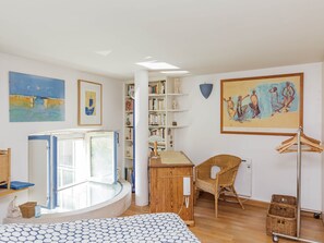 A room with a large window, a bookshelf, a wicker chair, and a painting on the wall.