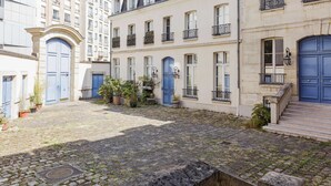 A courtyard with cobblestone pavement, a blue door, and a building with multiple windows and balconies. - Appt With Garden Near Jardin Du Luxembourg (Paris)