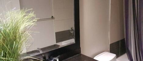A bathroom with a black countertop, a white sink, a mirror, a shower curtain, and a potted plant.