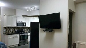Eine kleine Küche mit weißen Schränken, einer Mikrowelle und einem Backofen. Ein Flachbildfernseher ist an der Wand befestigt.
