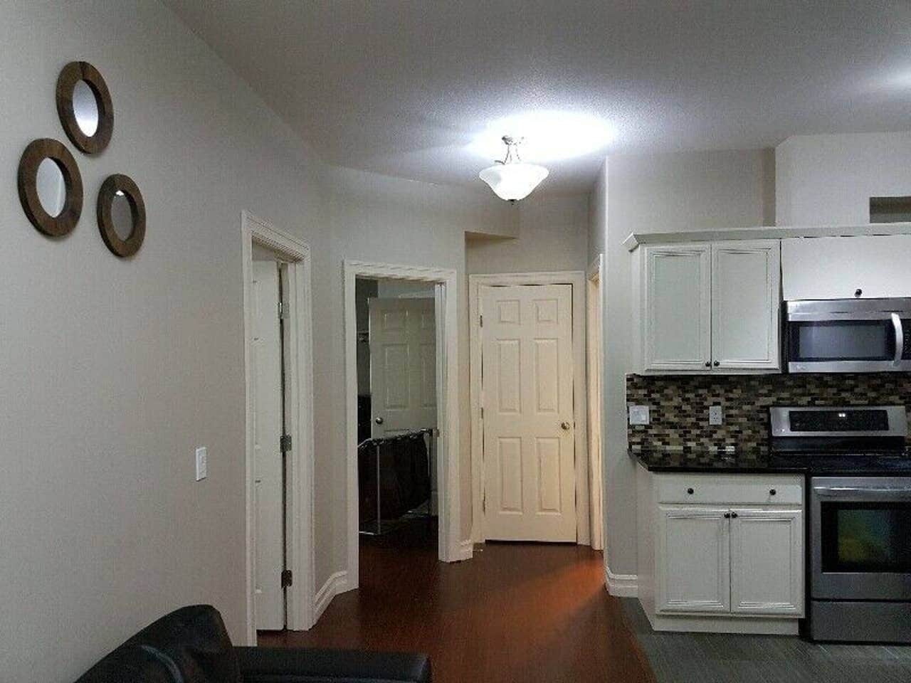 A compact kitchen with white cabinets, a microwave, and an oven. There is a hallway leading to another room.