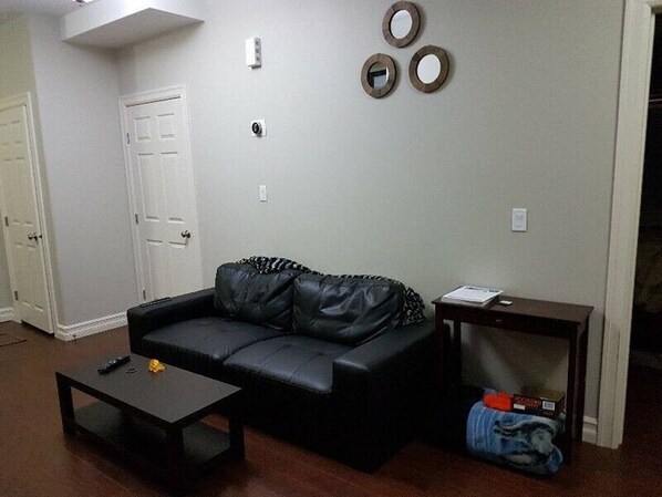 Sala de estar con un sofá de cuero negro, una mesa de centro y una mesita auxiliar de madera. Hay tres espejos circulares fijos a la pared y una puerta blanca.