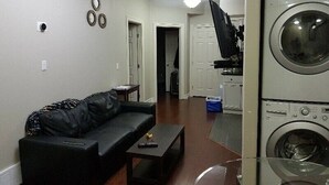 A living room with a black sofa, a coffee table, and a washing machine in the background.