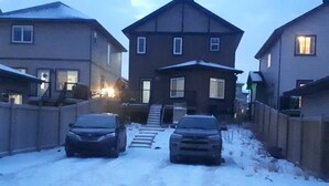 A residential street with two cars parked on the left and a staircase leading to a house.