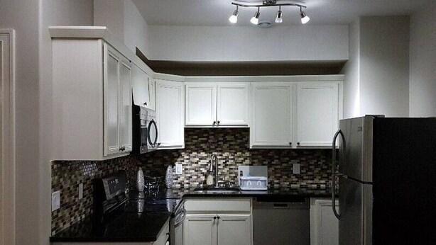 A kitchen with white cabinets, a black countertop, a microwave, a toaster, and a refrigerator.
