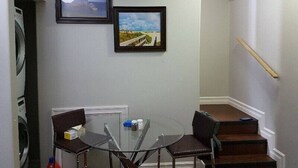 A small room with a glass table and two chairs, a staircase, and two framed pictures on the wall.