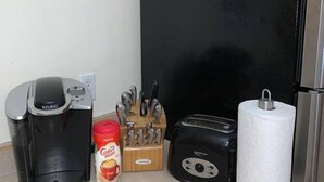 En köksbänk med en kaffebryggare, en brödrost, en hållare för hushållspapper, ett knivställ och en kaffemugg.
