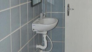 Un baño con lavamanos pedestal blanco, inodoro y paredes con azulejos.