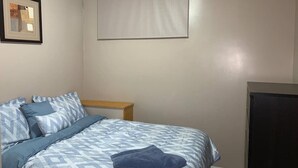 A bedroom with a bed, a wooden nightstand, a TV, and a window with a blind.