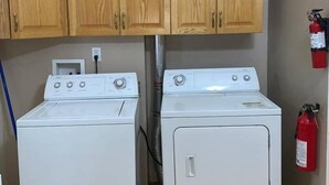 A laundry room with two white washing machines, wooden cabinets above, and a fire extinguisher on the wall.
