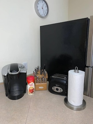 A kitchen counter with a coffee maker, a toaster, a paper towel holder, a knife block, and a coffee mug.