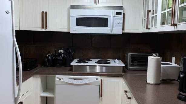 A compact kitchen with white cabinetry, a built-in microwave, a stove, and a dishwasher. - FLEETWOOD :1 Bedroom Space B1 (Fort McMurray)