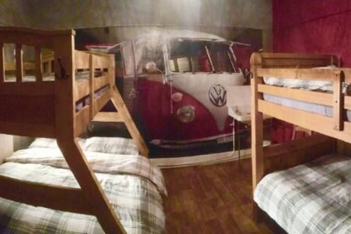 A room with bunk beds, a red Volkswagen camper van mural, and a red curtain.