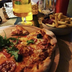 A pizza with toppings, a glass of beer, and a bowl of fries on a wooden table. - The Vagabond Bunkhouse & Pizzaria - Hostel (Betws-Y-Coed)