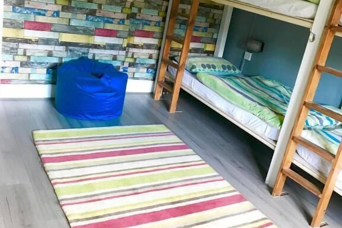A room with a bunk bed, a blue bean bag chair, a striped rug, and a multicolored brick wall.