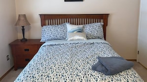 A bedroom with a wooden headboard, a bed with patterned bedding, a bedside lamp, and a framed picture on the wall. - TOP WOOD 4 Bedroom House (Fort McMurray)