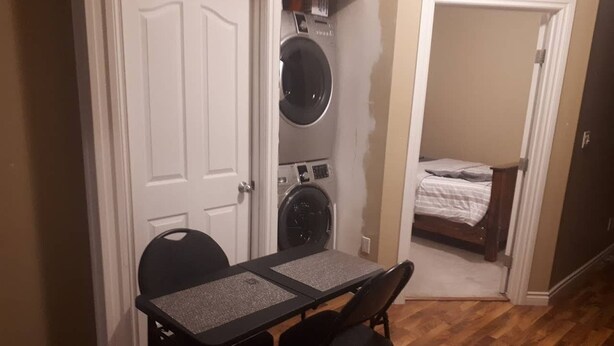 Habitación compacta con una pequeña mesa, sillas, lavadora y cama.