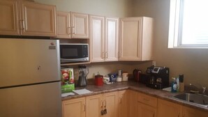 Una cocina con armarios de madera, un refrigerador, un microondas, una cafetera y varios utensilios de cocina sobre la encimera.