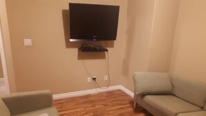 Una sala de estar con una televisión de pantalla plana montada en la pared, piso de madera y dos sofás.