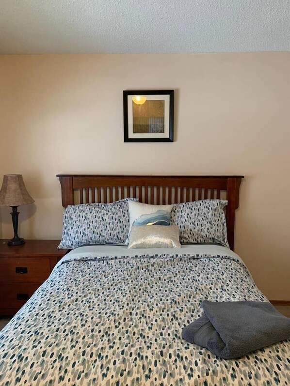 A neatly made bed with patterned bedding, a wooden headboard, and a bedside lamp.