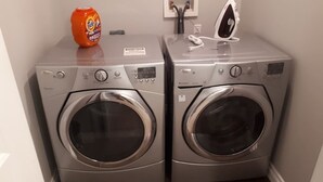 Two front-loading washing machines in a corner with a Tide detergent bottle on top.