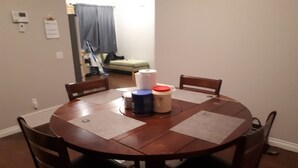 A round wooden dining table with four chairs, a small table lamp, and a few rolled-up papers on placemats.