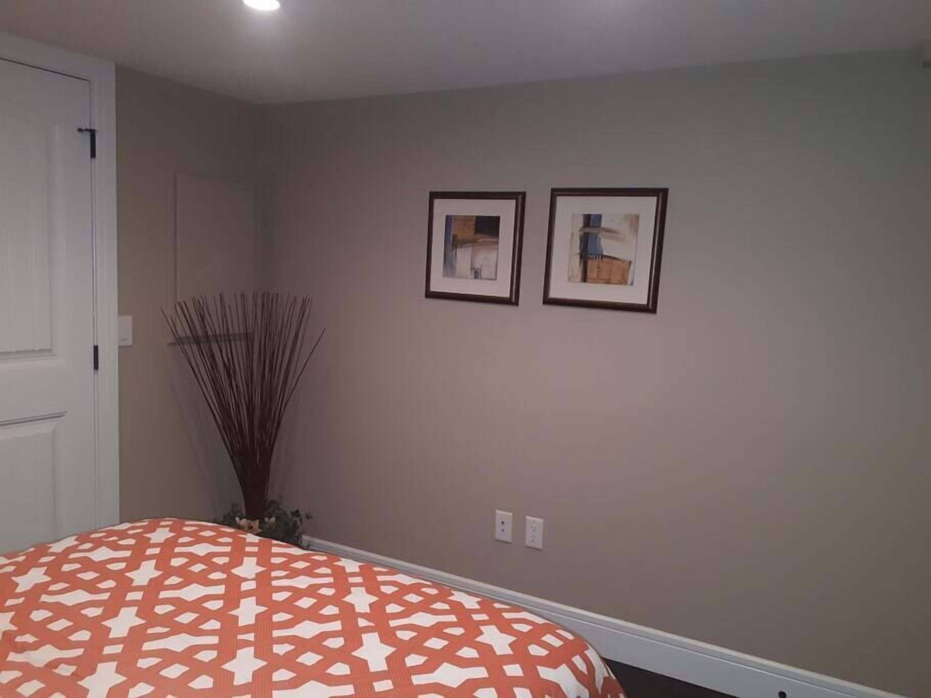 Een slaapkamer met een bedovertrek met een patroon, een witte deur en twee ingekaderde foto's aan de muur.