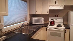 A kitchen with a stainless steel sink, a white microwave, a red kettle, a white stove, and a white refrigerator.
