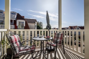 Een balkon met twee stoelen en een tafel, een wit hek en gebouwen op de achtergrond.