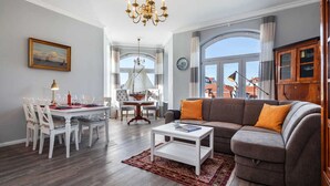 A spacious living room with a gray sofa, a white coffee table, and a dining area with a white table and chairs. - App. Lolita - Lolita (Kühlungsborn)