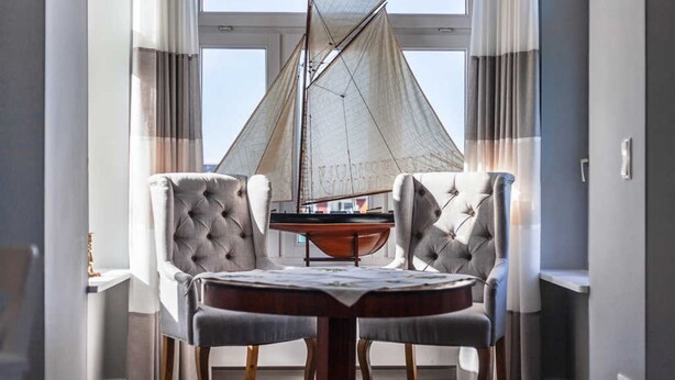 A dining area with a round table, two upholstered chairs, and a sailboat model. - App. Lolita - Lolita (Kühlungsborn)