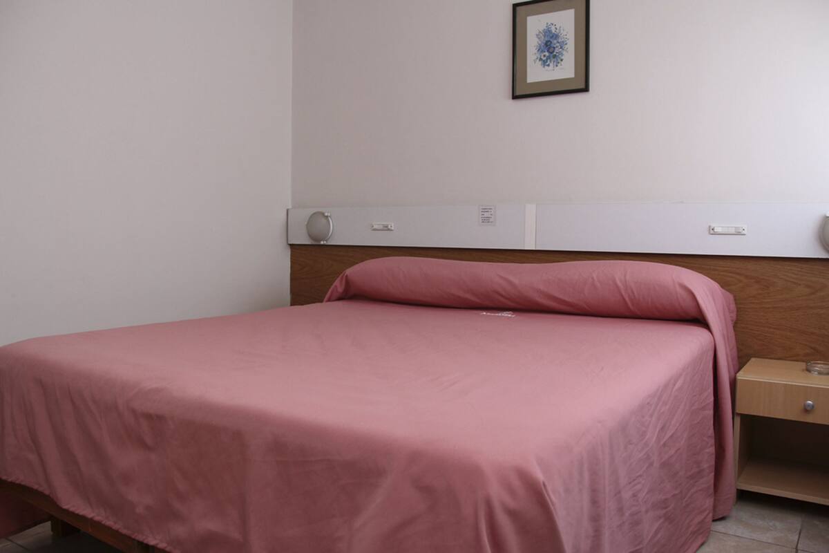 Una cama individual con colcha rosa en una habitación con paredes blancas y cabecera de madera.