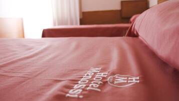 A hotel bed with a red bedspread and a logo that reads "Hotel Menotti."